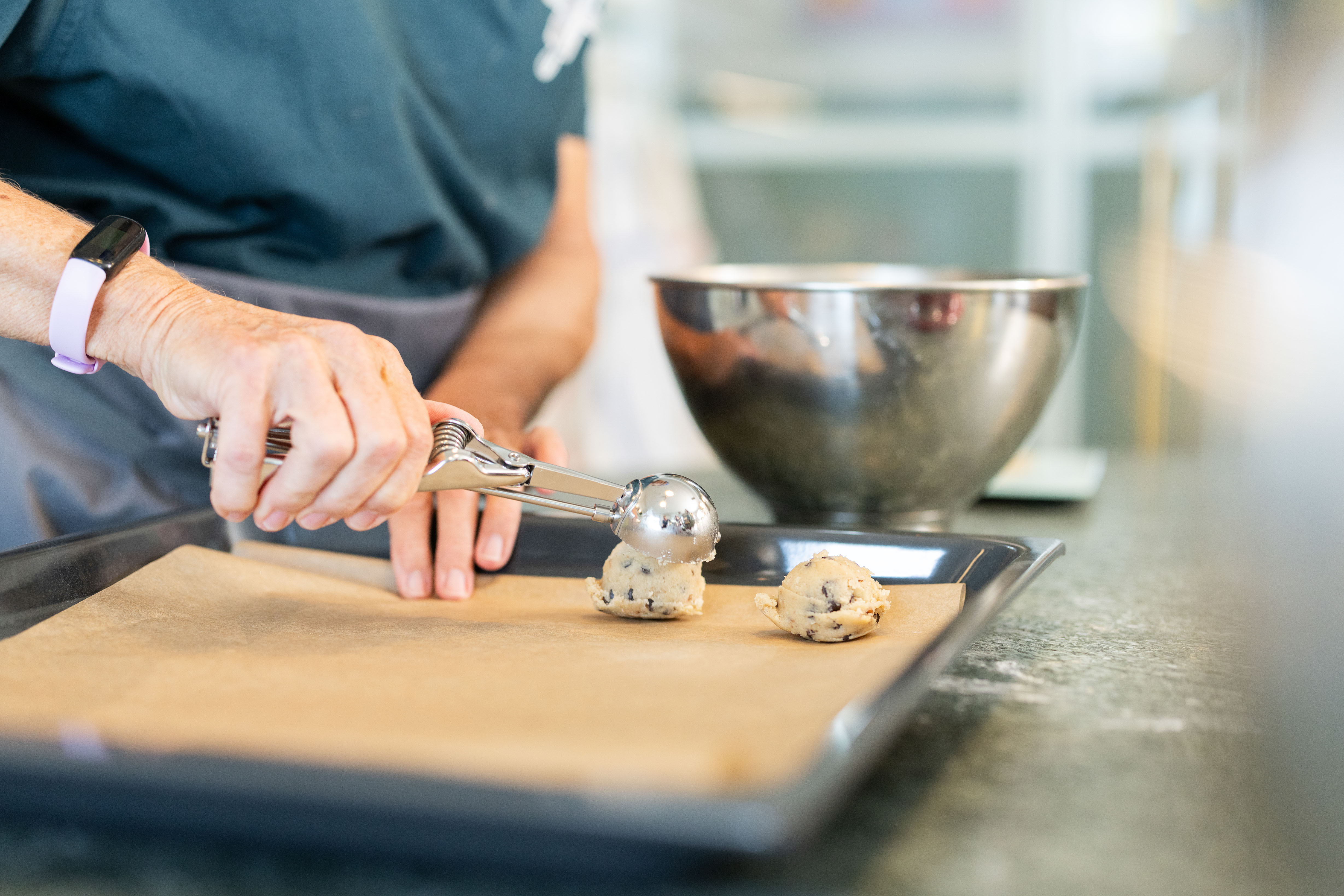 Nahaufnahme eines Eisportionierers, aus welchem sich eine geformte Kugel aus Cookieteig löst.