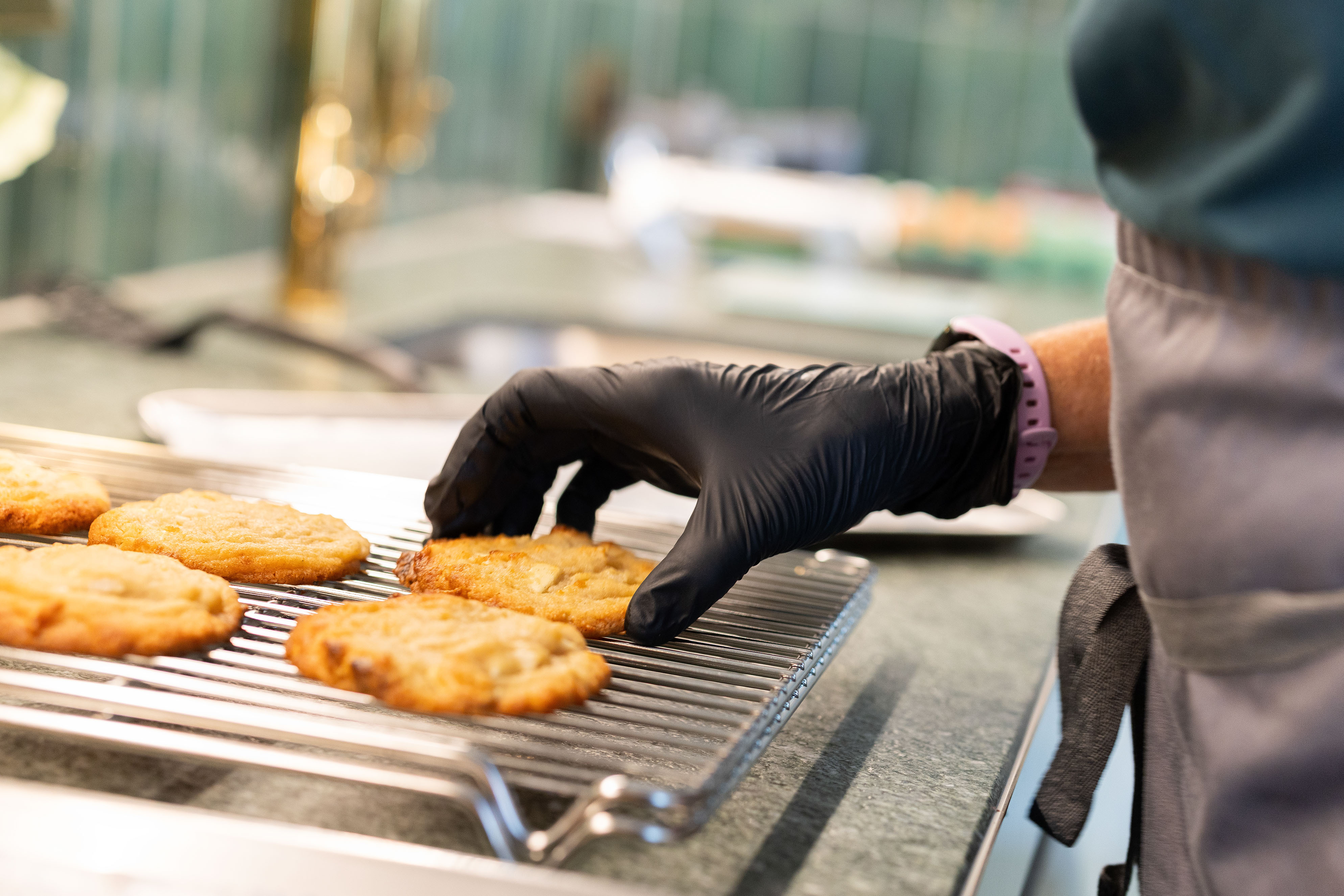 Cookies frisch aus dem Ofen auf einem Kühlgitter. Eine Hand in einem schwarzen Handschuh nimmt ein Cookie weg.