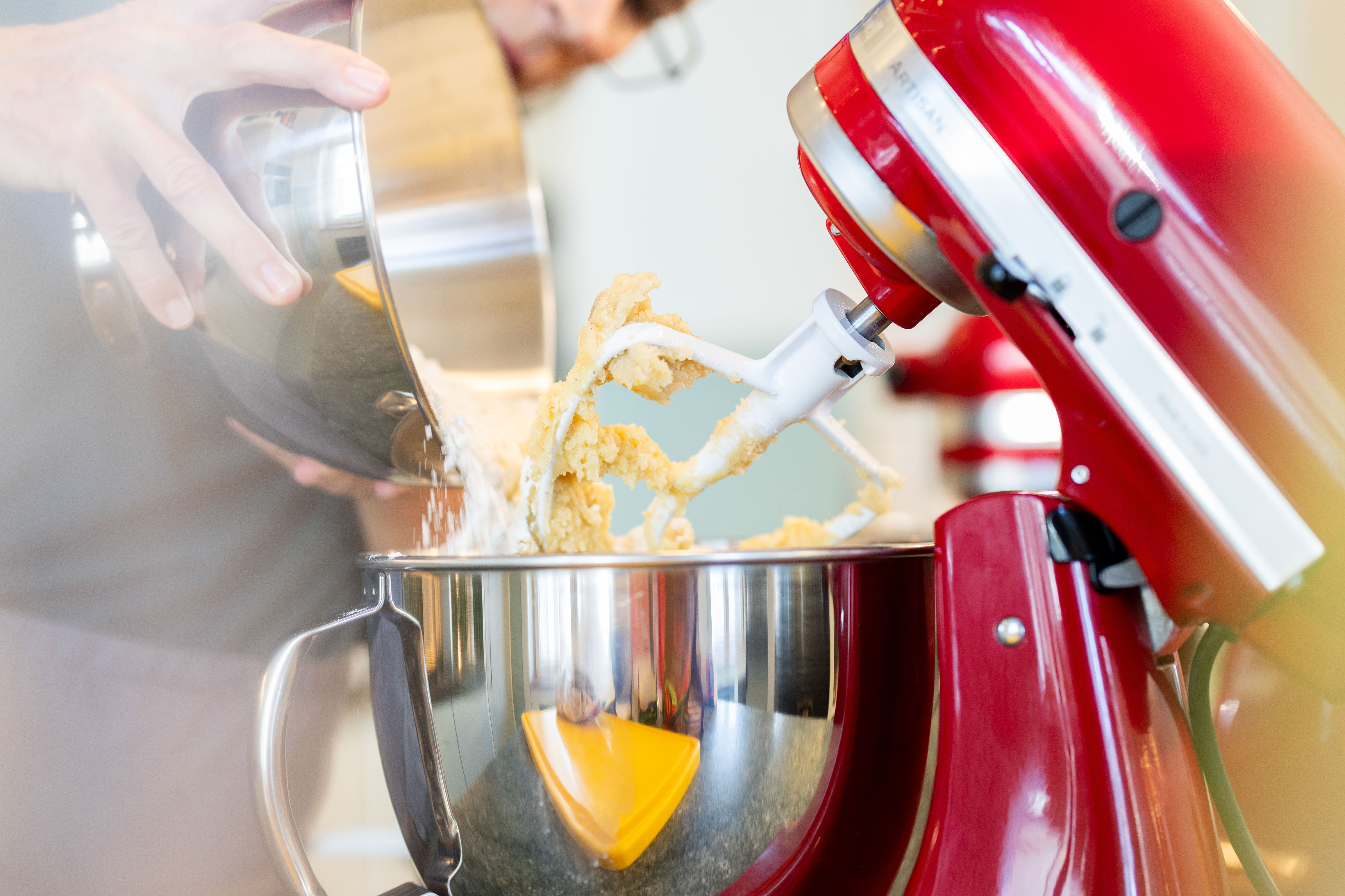 Nahaufnahme einer roten Küchenmaschine, Bäcker:in schüttet Mehl in die Schüssel. Teigproduktion