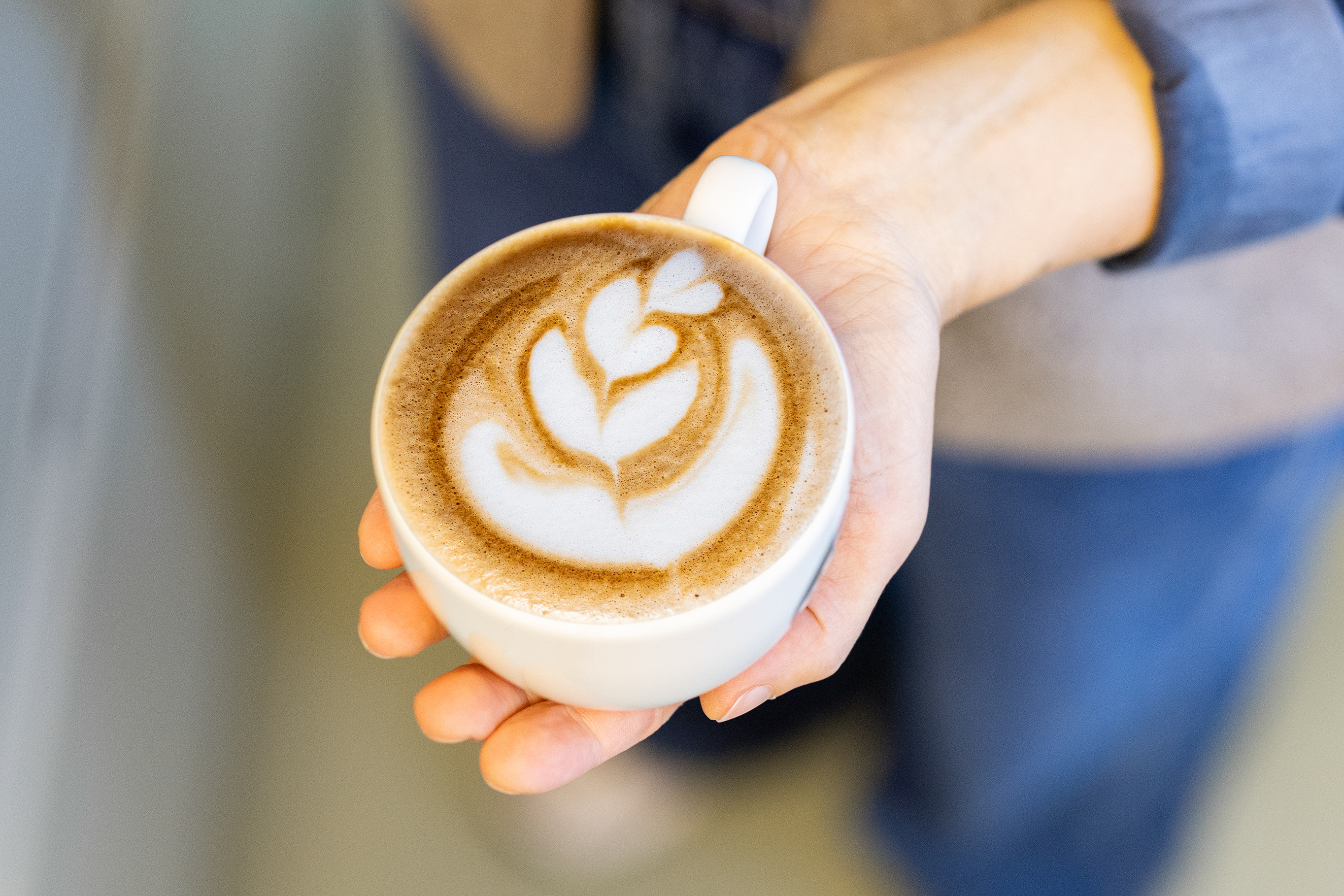 Nahaufnahme einer Kaffeetasse, Cappuccino von oben mit Latte-Art. Die Tasse wird in einer Hand gehalten.