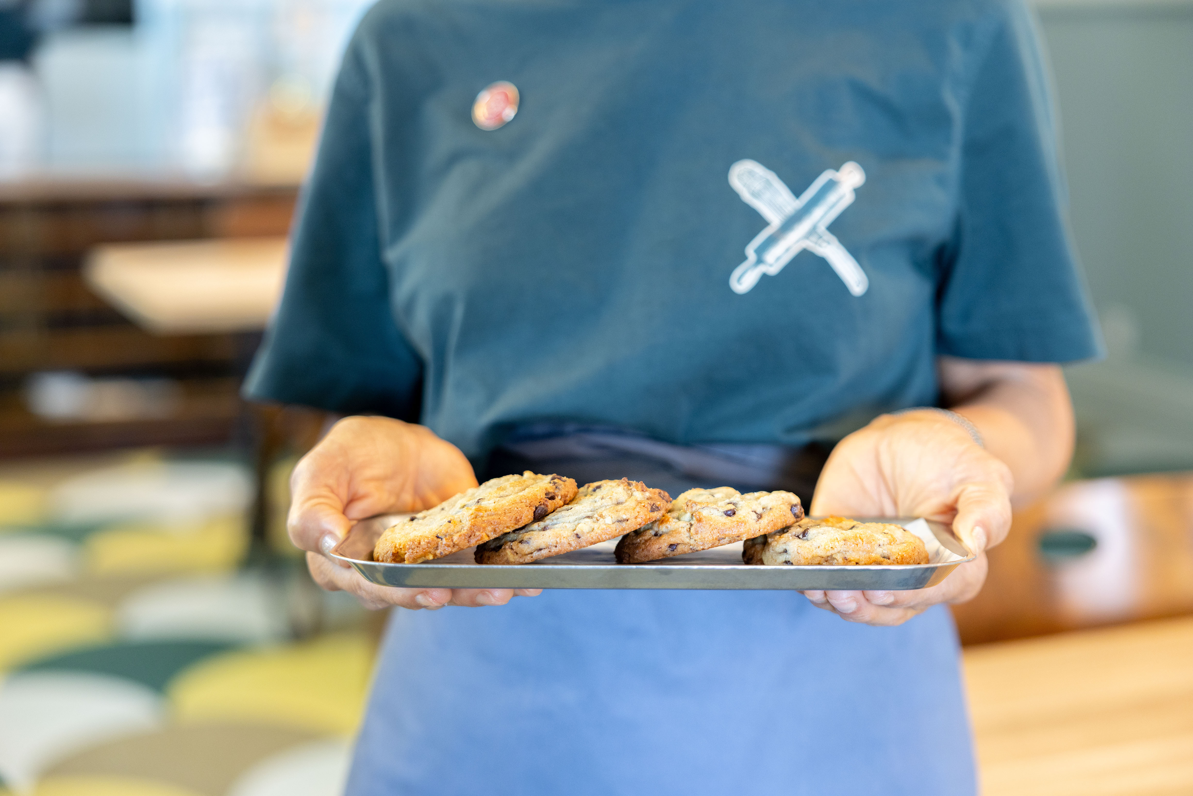 Frontalansicht eines Serviertabletts mit Cookies darauf. Das Tablett wird von einer Service-Person gehalten.